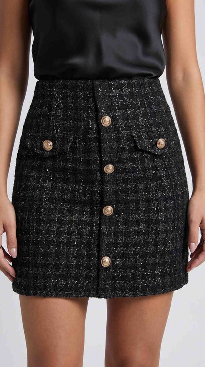 Fustă scurtă din tweed negru pentru femei, cu design elegant, buzunare decorative și nasturi aurii, creată pentru un look sofisticat și feminin. Ideală pentru ținute office, business, elegante și casual, fiind ușor de combinat cu sacouri, bluze și încălțăminte cu toc.