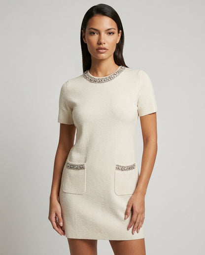 Rochie tricotată crem pentru damă, cu buzunare decorative accesorizate cu cristale strălucitoare și croială dreaptă elegantă. Rochie casual chic pentru femei, perfectă pentru birou, întâlniri, ieșiri în oraș și ținute elegante de zi.
