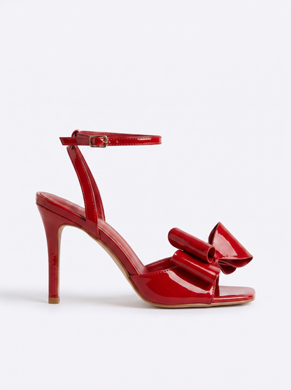 Sandale elegante damă roșii cu finisaj lucios, toc înalt de 9,5 cm, fundă decorativă supradimensionată și baretă reglabilă la gleznă, perfecte pentru nunți, botezuri, petreceri, banchete și alte evenimente speciale, fotografiate din profil pe model.