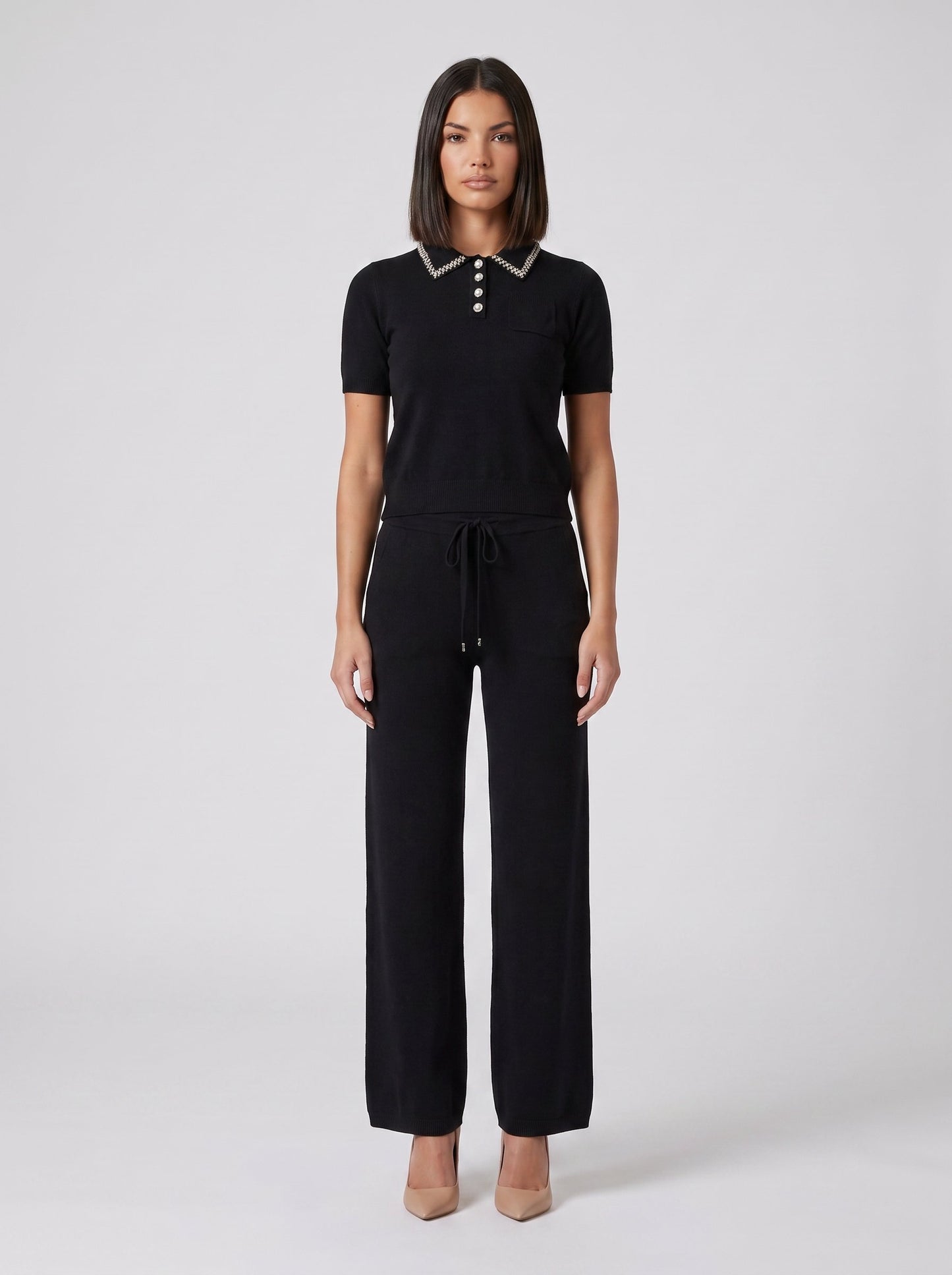Set tricot negru pentru damă, format din bluză lejeră cu detalii strălucitoare și pantaloni evazați cu talie elastică și șnur reglabil. Compleu elegant pentru femei, ideal pentru office, ieșiri în oraș, city break, vacanțe și ținute casual chic.