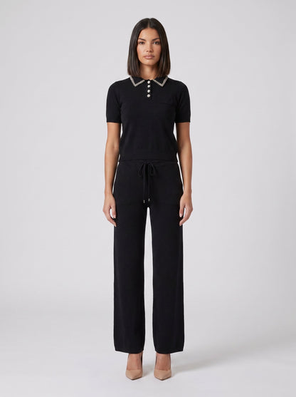 Set tricot negru pentru damă, format din bluză lejeră cu detalii strălucitoare și pantaloni evazați cu talie elastică și șnur reglabil. Compleu elegant pentru femei, ideal pentru office, ieșiri în oraș, city break, vacanțe și ținute casual chic.