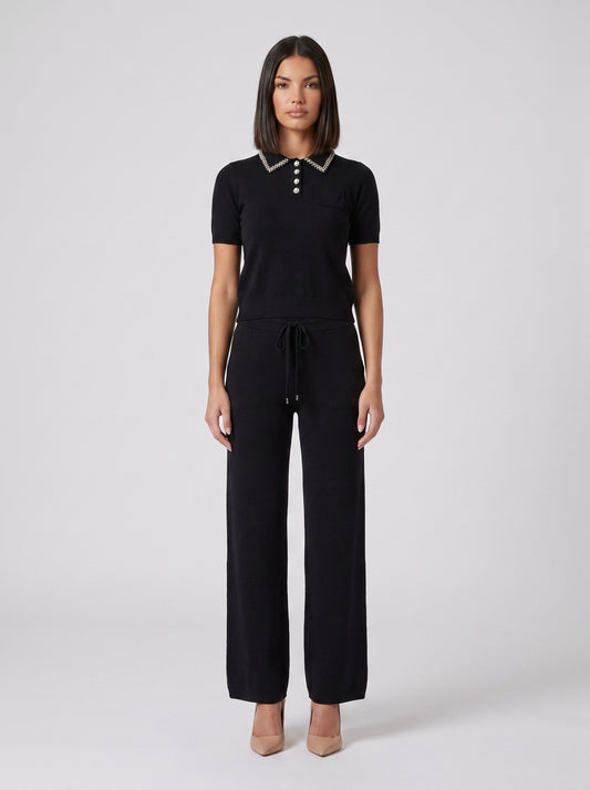 Set tricot negru pentru damă, format din bluză lejeră cu detalii strălucitoare și pantaloni evazați cu talie elastică și șnur reglabil. Compleu elegant pentru femei, ideal pentru office, ieșiri în oraș, city break, vacanțe și ținute casual chic.