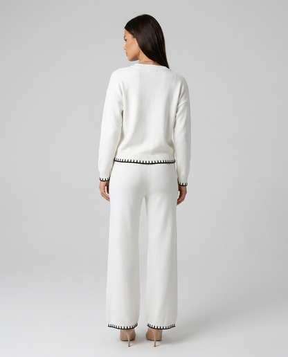 Compleu tricotat alb de damă cu bluză lejeră și pantaloni lungi confortabili, finisaje contrastante și material moale premium, perfect pentru ținute casual chic, relaxare, birou în stil smart casual, vacanțe și ieșiri în oraș.